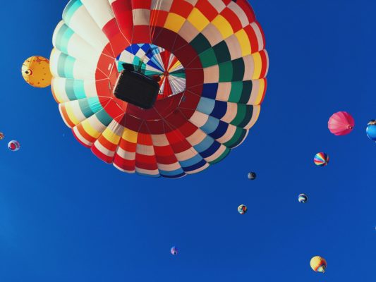 Heißluftballon von unten vor einem blauen Himmel und weiteren Heißluftballons in der Ferne