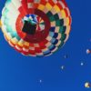 Heißluftballon von unten vor einem blauen Himmel und weiteren Heißluftballons in der Ferne