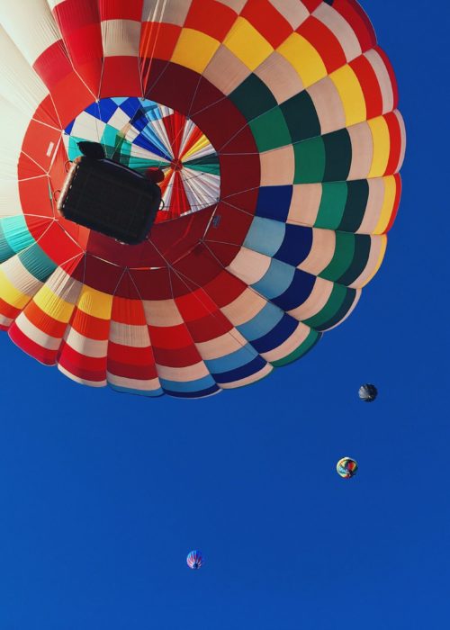 Heißluftballon von unten vor einem blauen Himmel und weiteren Heißluftballons in der Ferne